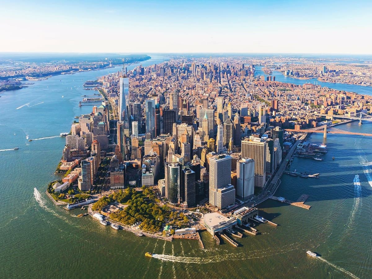 Aerial view of Lower Manhattan and surrounding waterways on a bright, clear sunny day.